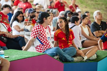 Audience members sit. Two in foreground wear soccer jerseys for Croatia and Spain.