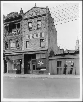 Image depicts facade of three storey brick structure, with shopfront on ground floor.