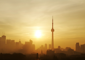 Smoggy cityscape with bright orange sun, CN Tower and buildings in background.