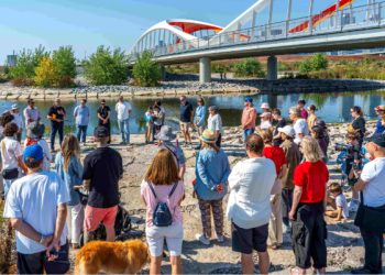 A group of people standing outside near a river watching a presentation