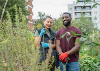 Two people standing in a field with gardening tools with apartment buildings in background.