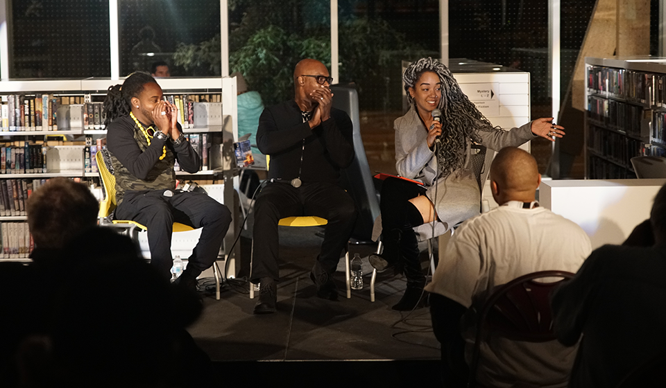 Three speakers talk on stage in front of audience