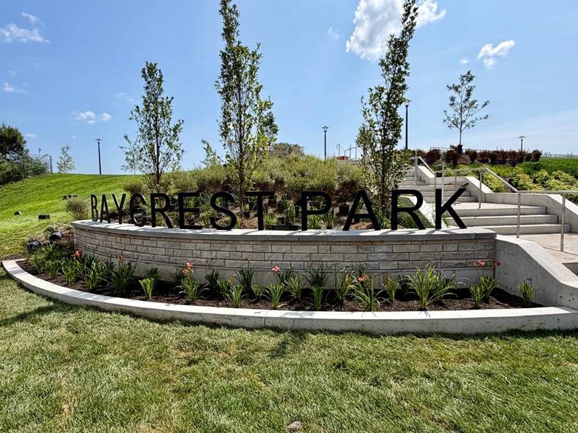The completed park sign, featuring "Baycrest Park" in black lettering mounted on a wall, with plantings in front.