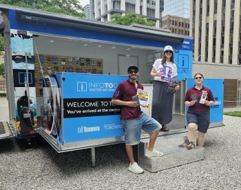 Three people standing in front of a pop-up trailers branded with "INFOTOGO" signs holding up pamphlets and posters.