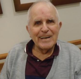 Peter sits and smiles, wearing a gray sweater and red collared shirt beneath it.