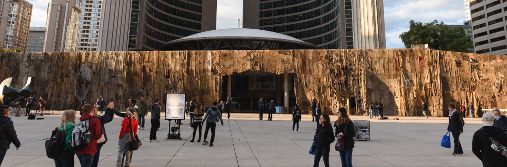 People walking across Nathan Phillips Square and City Hall covered in an artwork. Rotunda and towers behind.