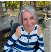 Doreen smiles while seated in a courtyard, wearing a white and blue striped shirt.