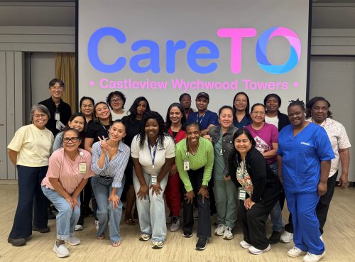 21 staff pose for a photo in front of a projector screen that says CareTO Castleview Wychwood Towers