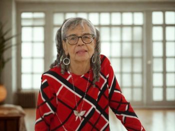 Emelia sits in a brightly lit room with lots of windows, wearing a red checked sweater