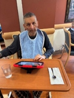 A resident sits at a wooden table wearing a blue bib and using an iPad.