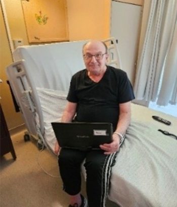 A resident sits on the edge of their bed and holds a portable DVD player.