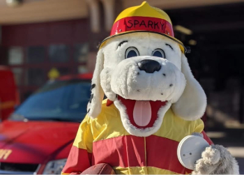 Sparky the Fire Dog mascot holding a fire alarm.