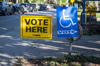 Vote Here” and accessible voting signs beside a sidewalk outside a polling location.