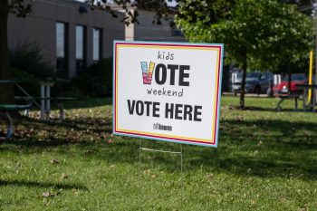 Colourful lawn sign reading “Kids Vote Weekend - VOTE HERE” with the City of Toronto logo, displayed on grass outside a voting place.
