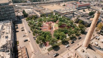 Aerial rendering showing a new urban park with extensive tree canopy, gathering spaces, and a central landmark structure framed by surrounding heritage industrial buildings.