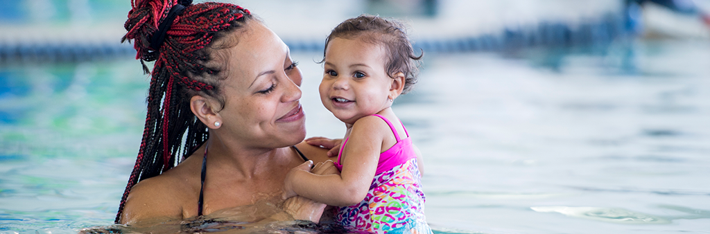 A person holding a small child in a pool.