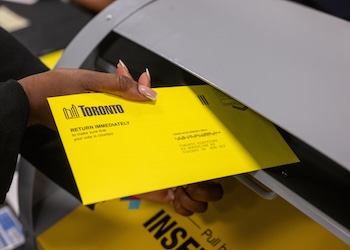 A person placing a yellow mail-in vote into the mailbox.