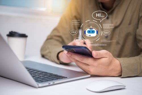 A person is accessing information on their mobile phone while sitting in front of a laptop.