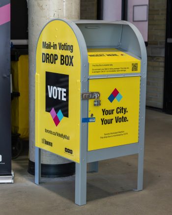 Yellow and grey City of Toronto mail-in voting drop box. Provide your feedback on BizChat