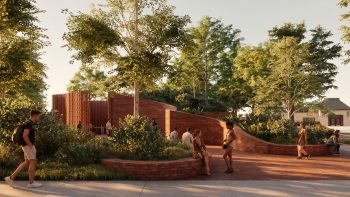 View of the park's planted landscape featuring curved brick walls, accessible pathways, seating areas, and the public washroom pavilion nestled within the terrain.