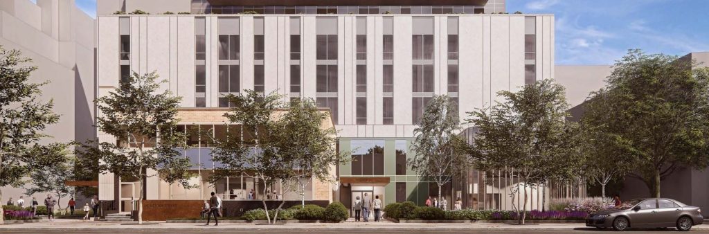 The base of a new apartment building with people walking outside the building and landscaped areas along the sidewalk.