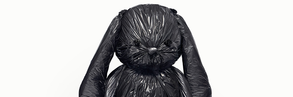 A stuffed bunny wrapped in a black garbage bag.