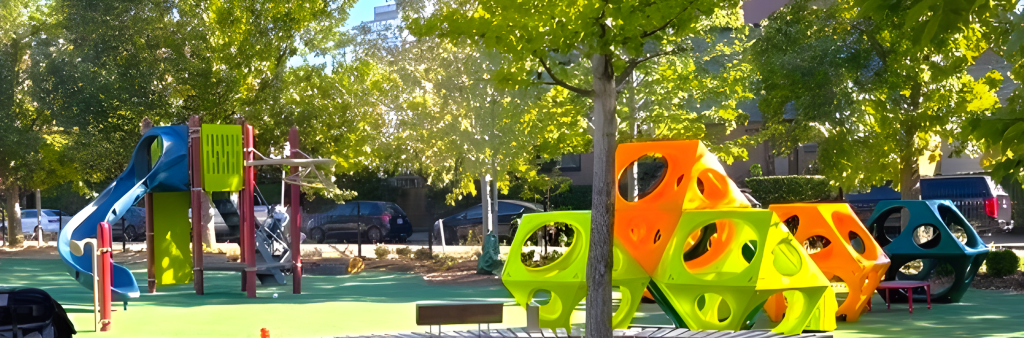 New Wychwood Barns Park playground showing a main play structure with two slides on the left and play cubes on the right with a circular bench in front.