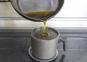 A frying pan pouring cooking oil into a pot with a strainer.
