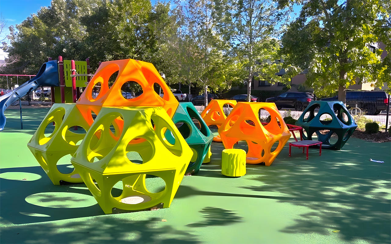 Close up of the new Wychwood Barns Park playground, showing the main play structure with two slides in the back and colourful play cubes in front.